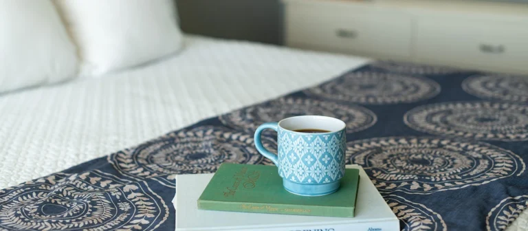 Morning coffee and books resting on a bed inside a cozy oceanfront guest room.