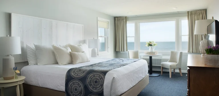 Upper building second- and third-floor king guest room with oceanfront seating nook, dresser, and coastal decor accents.