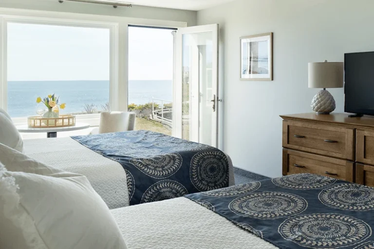 Bright upper building first-floor guest room with two beds, ocean views, and direct outdoor access.